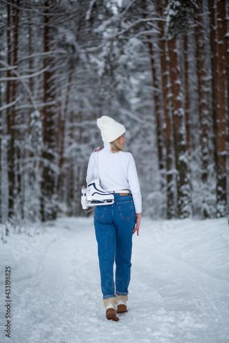 Young blond beautiful female with white ice skates in her hand in winter snowy forest.