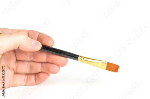 A man's hand holds paintbrush on a white background in close-up.