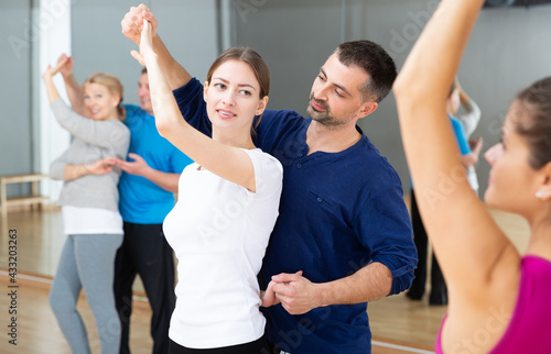 Young smiling woman and man practicing social dance moves in pair during group class