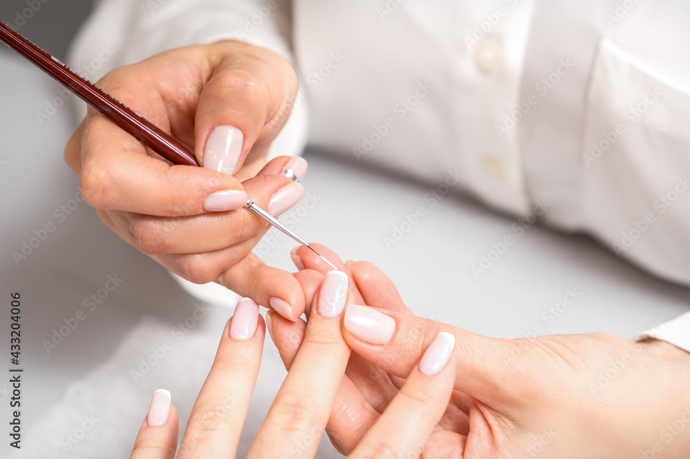 French manicure. Manicure master drawing white varnish on the nail tip with a thin brush, close up French manicure. Manicure master drawing white varnish on the nail tip with a thin brush, close up