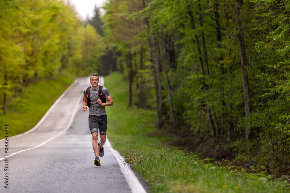 Sportsman mountain runner running on a road surrounded by a green forest