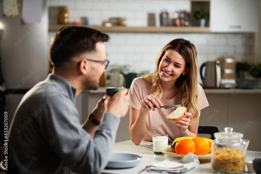 Beautiful young girl enjoying in breakfast with her boyfriend. Loving couple drinking coffee in the kitchen