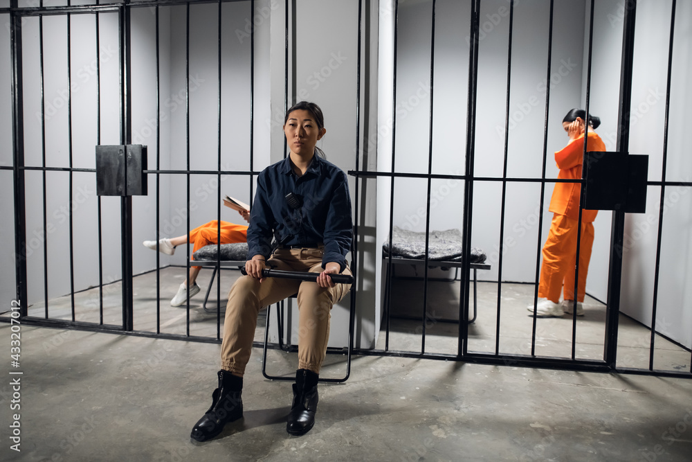 Fototapeta premium A typical day in a women's prison. A bored female guard in uniform sits near the cells with female prisoners.