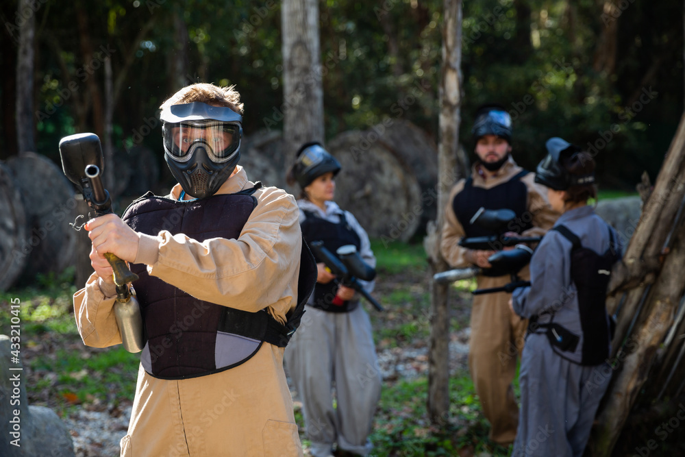 Fototapeta premium Portrait of male paintball sport player holding shooting gun and his team on background