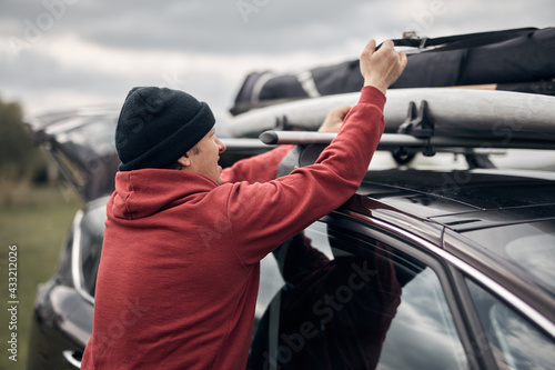 Windsurfer and camper packing and unpacking from a car's roof rack in nature.