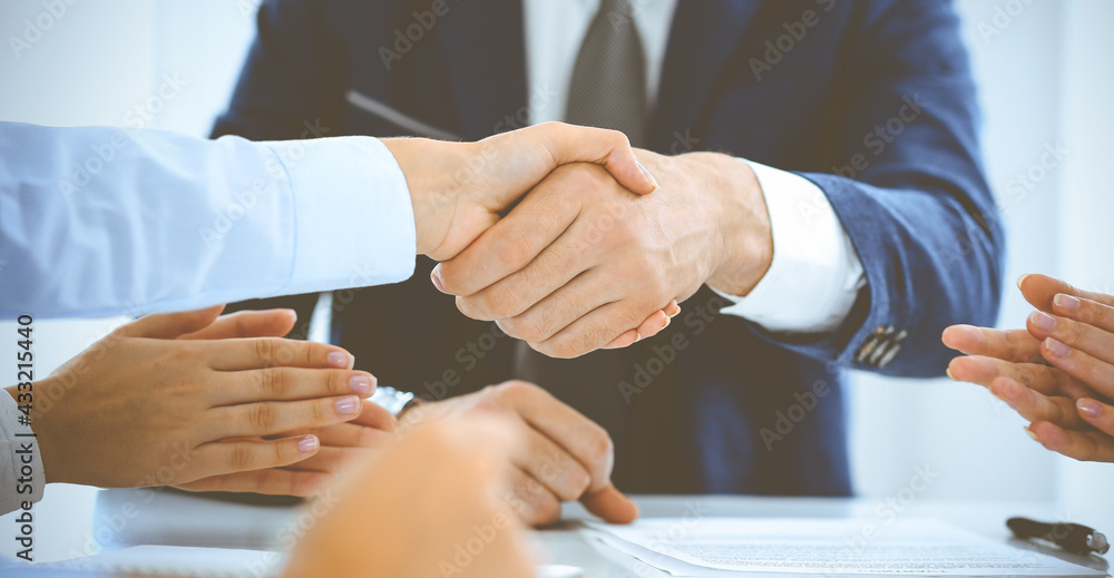 Businesspeople or lawyers shaking hands finishing up a meeting in blue toned office , close-up. Success at negotiation and handshake concepts