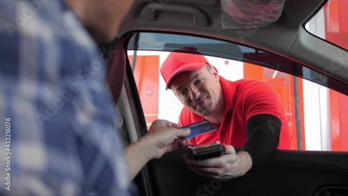 Hand of customer paying with contactless credit card with NFC technology to worker of gas station for payment terminal while sitting in the car, credit card reader machine. photo