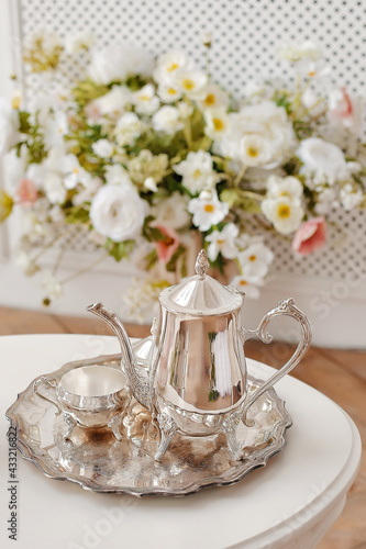Coffee table decorated with flowers. Silver teapot on a tray. Classic interior