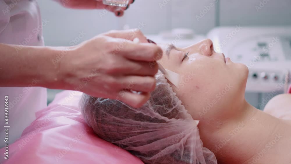 Peeling of skin face. Beautician applies peeling gel to client's face. Young woman at spa treatments. Close up. Slider shot. Peeling of skin face. Beautician applies peeling gel to client's face. Young woman at spa treatments. Close up. Slider shot.