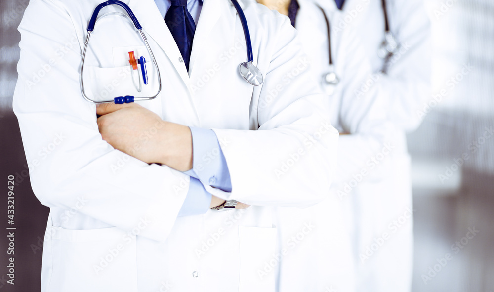 Group of modern doctors standing as a team with crossed arms and stethoscopes in hospital office. Physicians ready to examine and help patients. Medical help, insurance in health care, best desease Group of modern doctors standing as a team with crossed arms and stethoscopes in hospital office. Physicians ready to examine and help patients. Medical help, insurance in health care, best desease