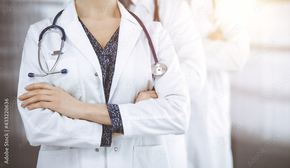 Doctors standing as a team with arms crossed in sunny clinic. Medical help, insurance and medicine concept Doctors standing as a team with arms crossed in sunny clinic. Medical help, insurance and medicine concept