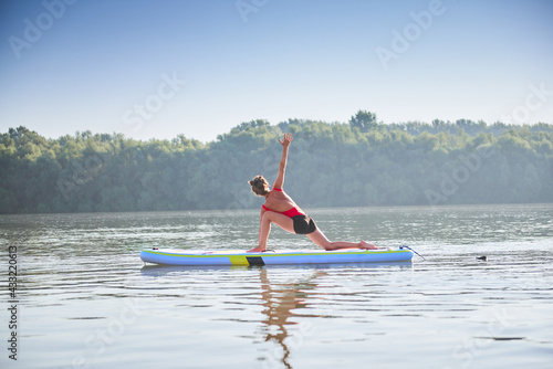 Woman in a extended triangle pose and practising yoga during on a paddleboard