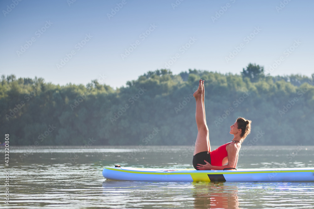 Woman meditating and practising yoga during sunrise in paddle board