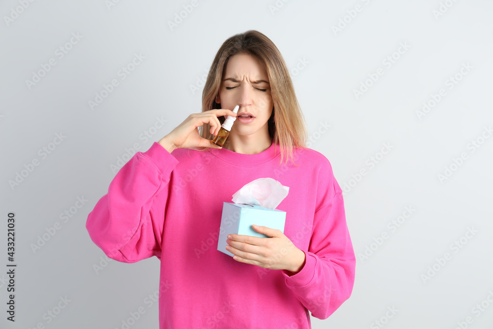 Sick young woman using nasal spray on white background Sick young woman using nasal spray on white background