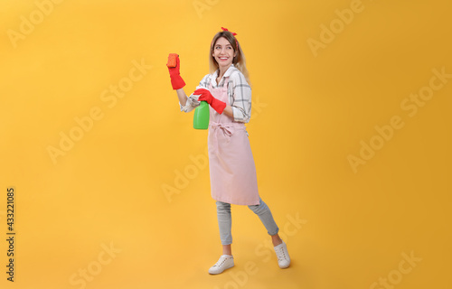 Young housewife with detergent and sponge on yellow background