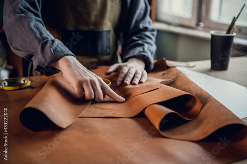 The initial stage of production of leather shoes  a young guy lays out the leather on the table for further use
