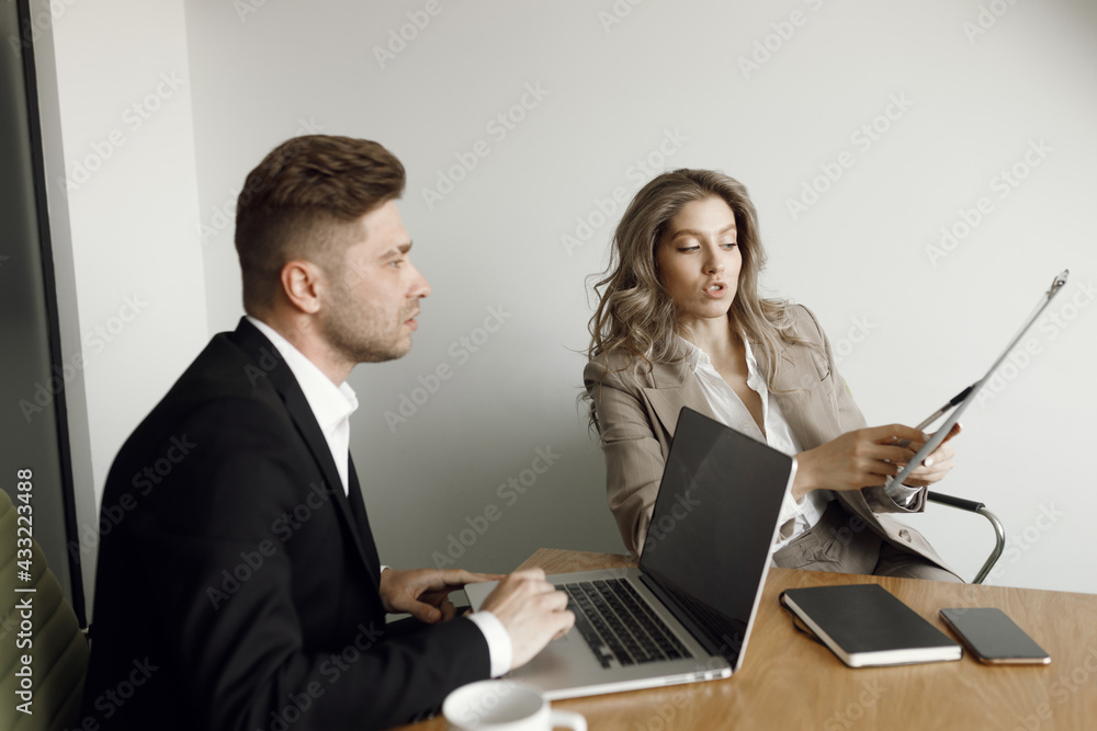 A couple working at a laptop and blueprints in their home office smile. A man and a woman discuss business matters. A couple working at a laptop and blueprints in their home office smile. A man and a woman discuss business matters.