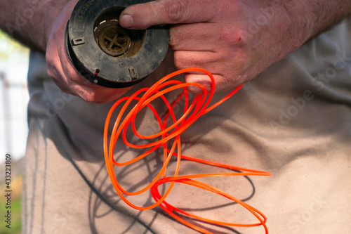 a man winds a new fishing line into the spool of a grass mowing trimmer