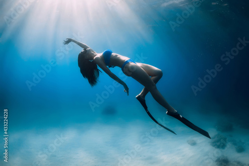 Attractive free diver woman with fins dive at deep underwater in sea.