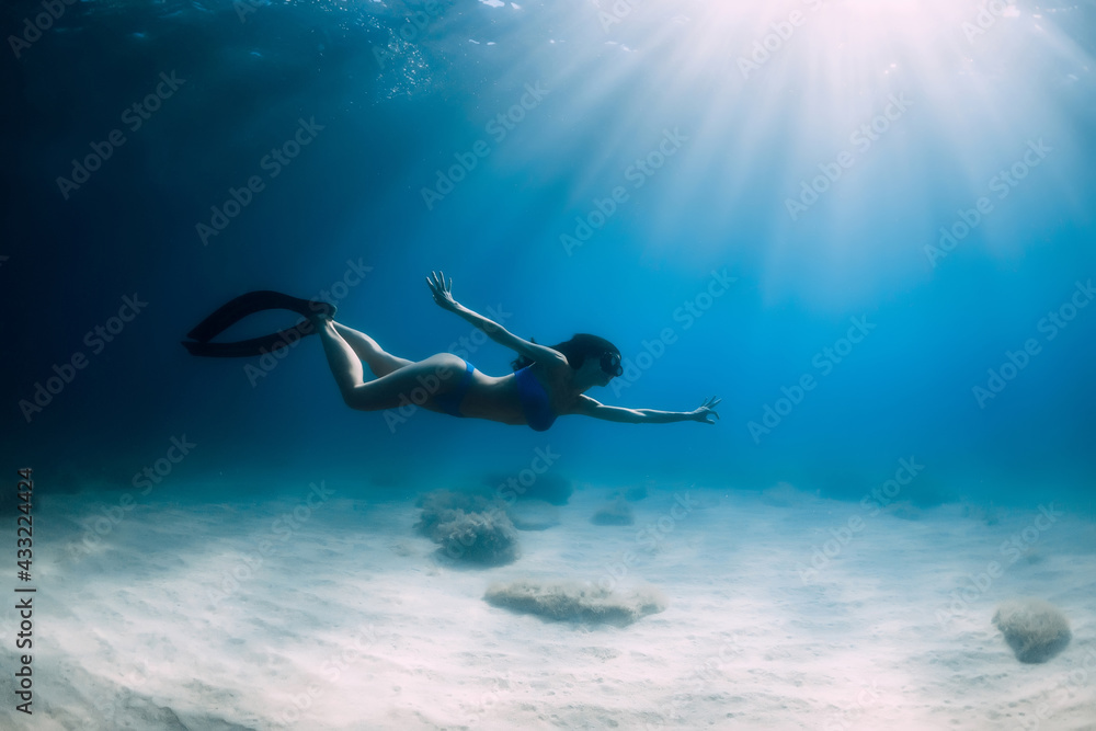 Attractive free diver woman with fins dive at deep underwater in sea.