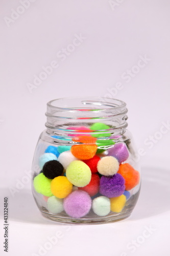 Colorful pompom in glass bottle on white background