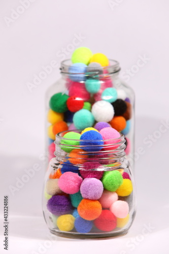 Colorful pompom in glass bottle on white background