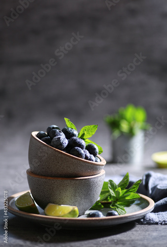 Fresh berries with drops, blueberries with lime, mint in a bowl on a gray background. Summer, freshness, sunshine. Background image, copy space