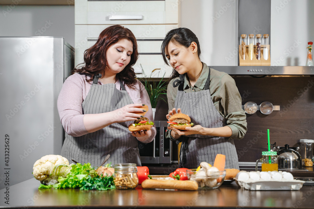 Two attractive young women preparing delicious burgers in the kitchen