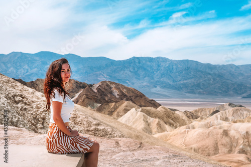 A beautiful young woman with long hair sits on a bench on a hot day in Death Valley Zabriskie Point, USA. © KseniaJoyg