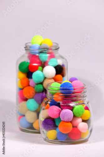 Colorful pompom in glass bottle on white background