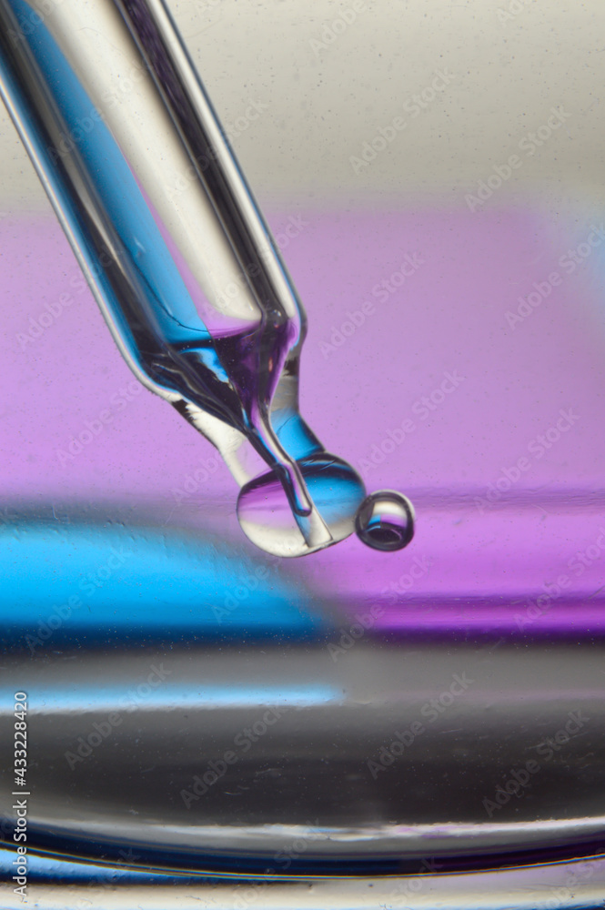 Cosmetic pipette with drops of transparent liquid and a jar, close-up on a colored background.