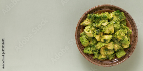 Bowl of freshly made chunky guacamole on bright green background with copy space for text, top view.