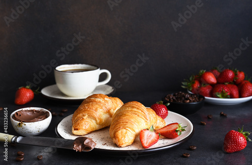 Croissant with chocolate paste and a cup of coffee, strawberries on the kitchen table. ​Traditional snack or breakfast.
