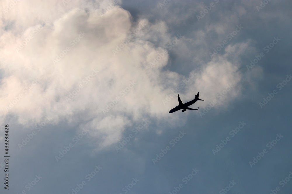 Black silhouette of airplane flying in the blue sky on background of white clouds. Twin-engine commercial plane, turbulence and travel concept Black silhouette of airplane flying in the blue sky on background of white clouds. Twin-engine commercial plane, turbulence and travel concept