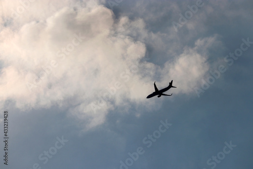 Black silhouette of airplane flying in the blue sky on background of white clouds. Twin-engine commercial plane, turbulence and travel concept