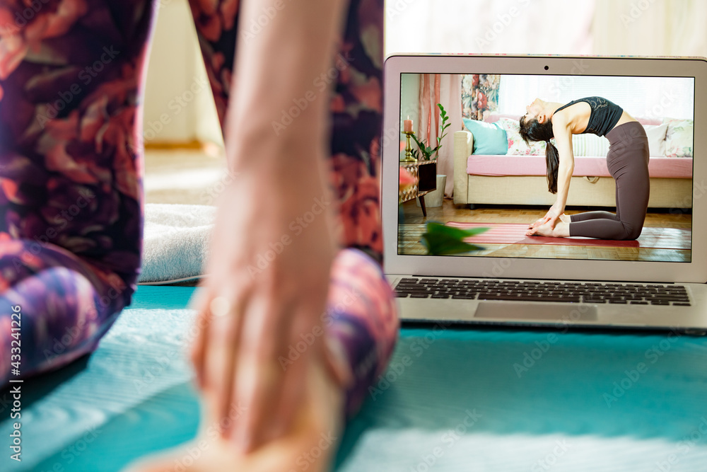 Naklejka premium Beautiful fit woman streaming broadcast video blog about yoga and fitness in living room. Healthy lifestyle and social media. Woman watching video tutorials on laptop and working out at home.