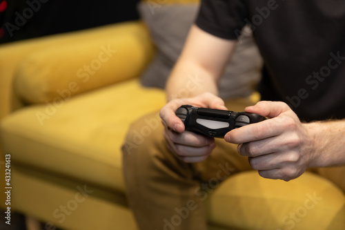 Hairy male hands holding joystick close up. guy intently Enjoying male console game. man Playing Videogame alone sitting on comfy yellow sofa Resting At Home. Loneliness, self-sufficiency concept