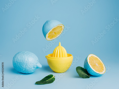 Fotografie Blue painted lemons with yellow juice squeezer and fresh leaves against pastel blue background