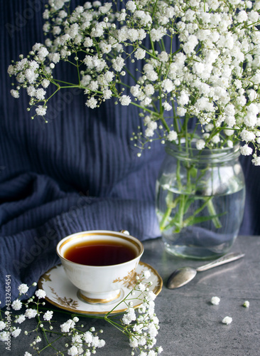Still life with cup of tea. Simple composition photo with small white flowers and cup of black tea on a table. Beautiful morning picture. 