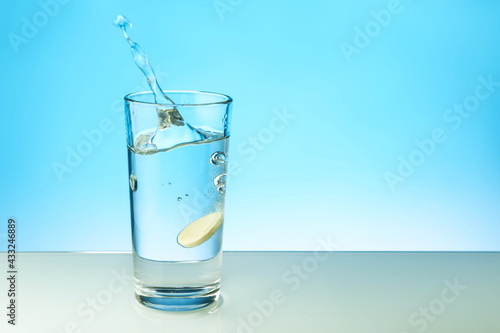 dissolving tablet dissolves in water on colored background. a glass of water and an effervescent vitamin pill. the medicine tablet dissolves in a glass of water