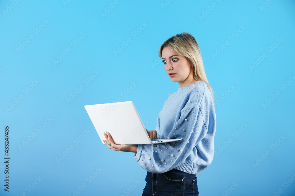 confused woman looking through laptop on colored background. young dumbfounded woman using laptop on a blue background. confused woman looking through laptop on colored background. young dumbfounded woman using laptop on a blue background.