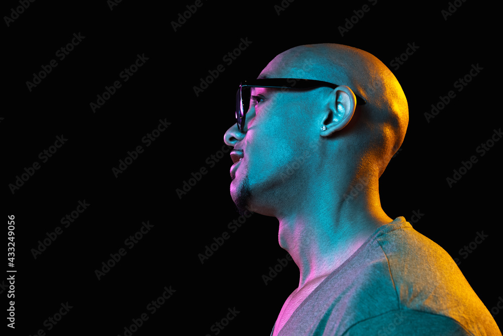 African-american young man's portrait on dark studio background in neon. Concept of human emotions, facial expression, youth, sales, ad.