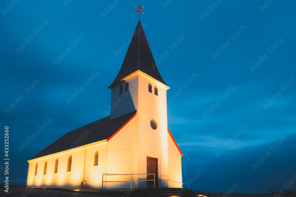Evening close-up view of an illuminated Reyniskyrka Church at night, a picturesque chapel in the southern Iceland coastal village of Vik.