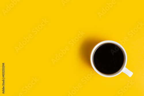 Top view of the white cup of coffee on the yellow background with a free space for text. Getting up early. Wake up with a great mood