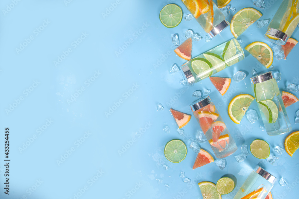 Variety of cold drinks in bottles, summer infused water bottles, lemonade healthy cocktails with different  citrus fruits - lemon, orange, grapefruit, lime, bright background copy space