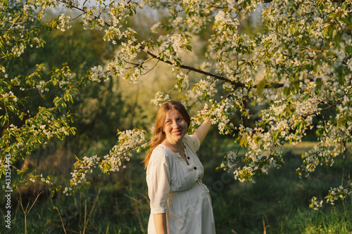 Spring portrait of a pregnant woman. A beautiful young pregnant woman in a white dress walks in the spring garden.