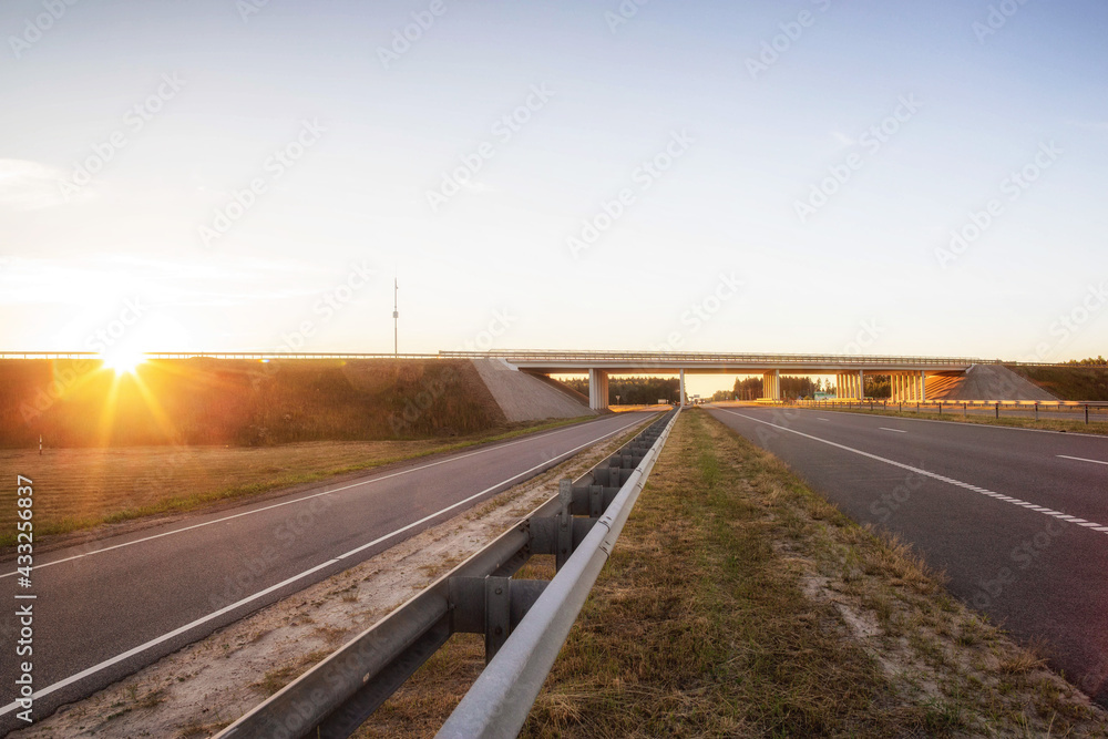 The highway is crossed by a bridge with a road against the backdrop of a sunny sunset. Engineering and architecture concept, copy space for text