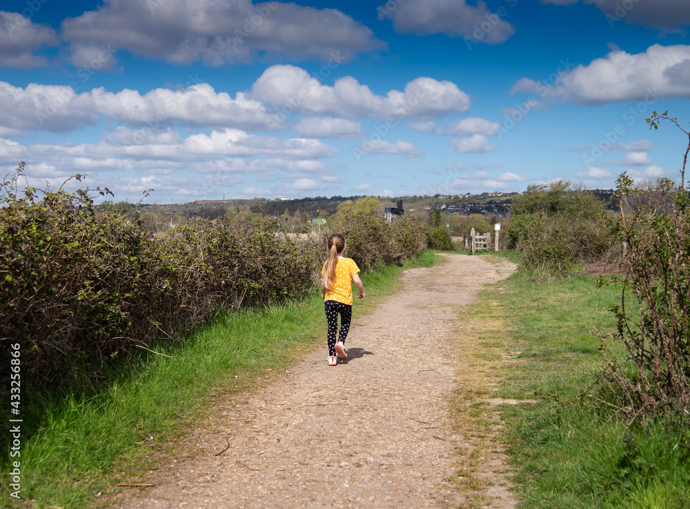 Backview of a young girl running along a gravel path at Farlington marshes, Portsmouth.
