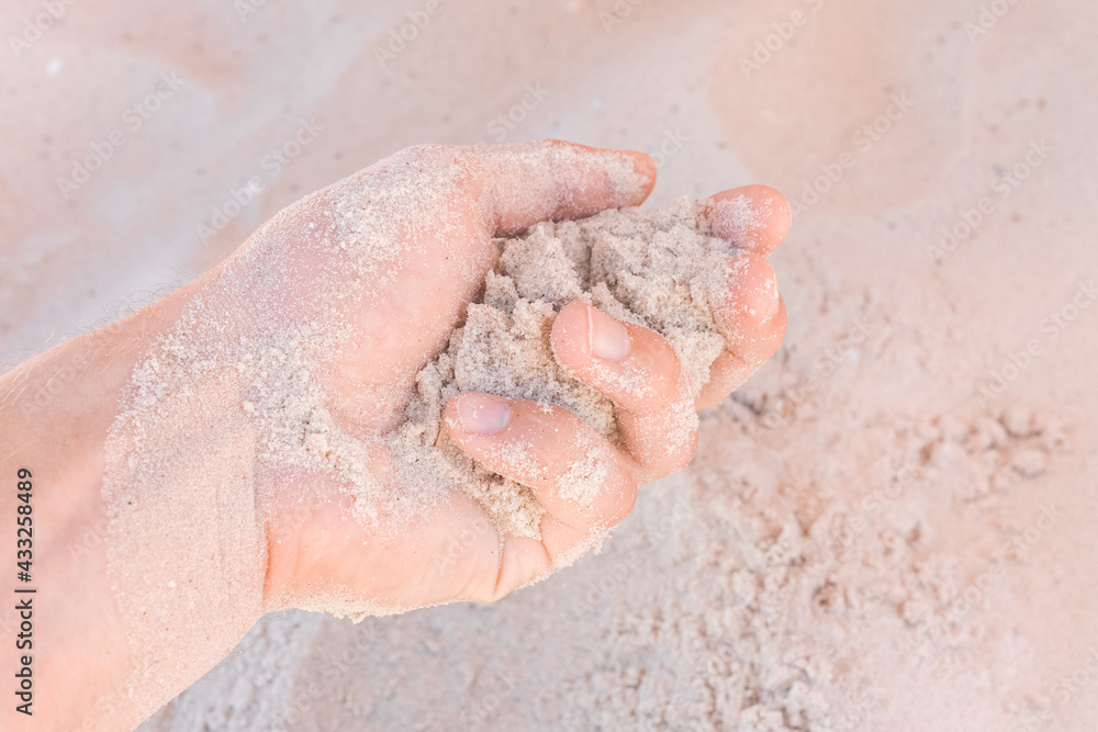 Fototapeta premium The guy's hand takes or touches the white beach sand close up