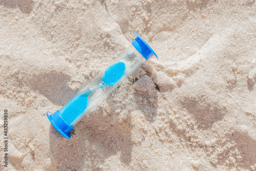The hourglass close-up lies on the light beach sand. The concept of time The hourglass close-up lies on the light beach sand. The concept of time